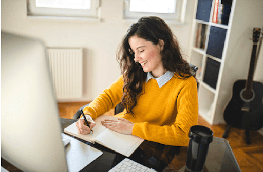 woman in a yellow sweater writing on a piece of paper at her table